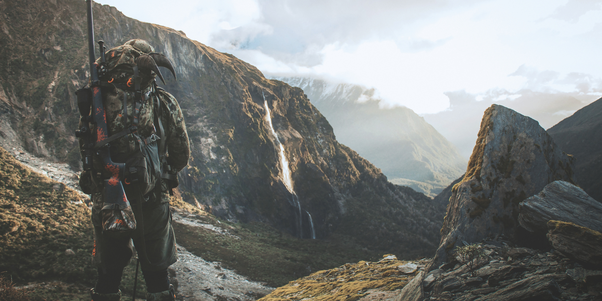Spika Rep in camouflage gear with a rifle standing on a mountain path